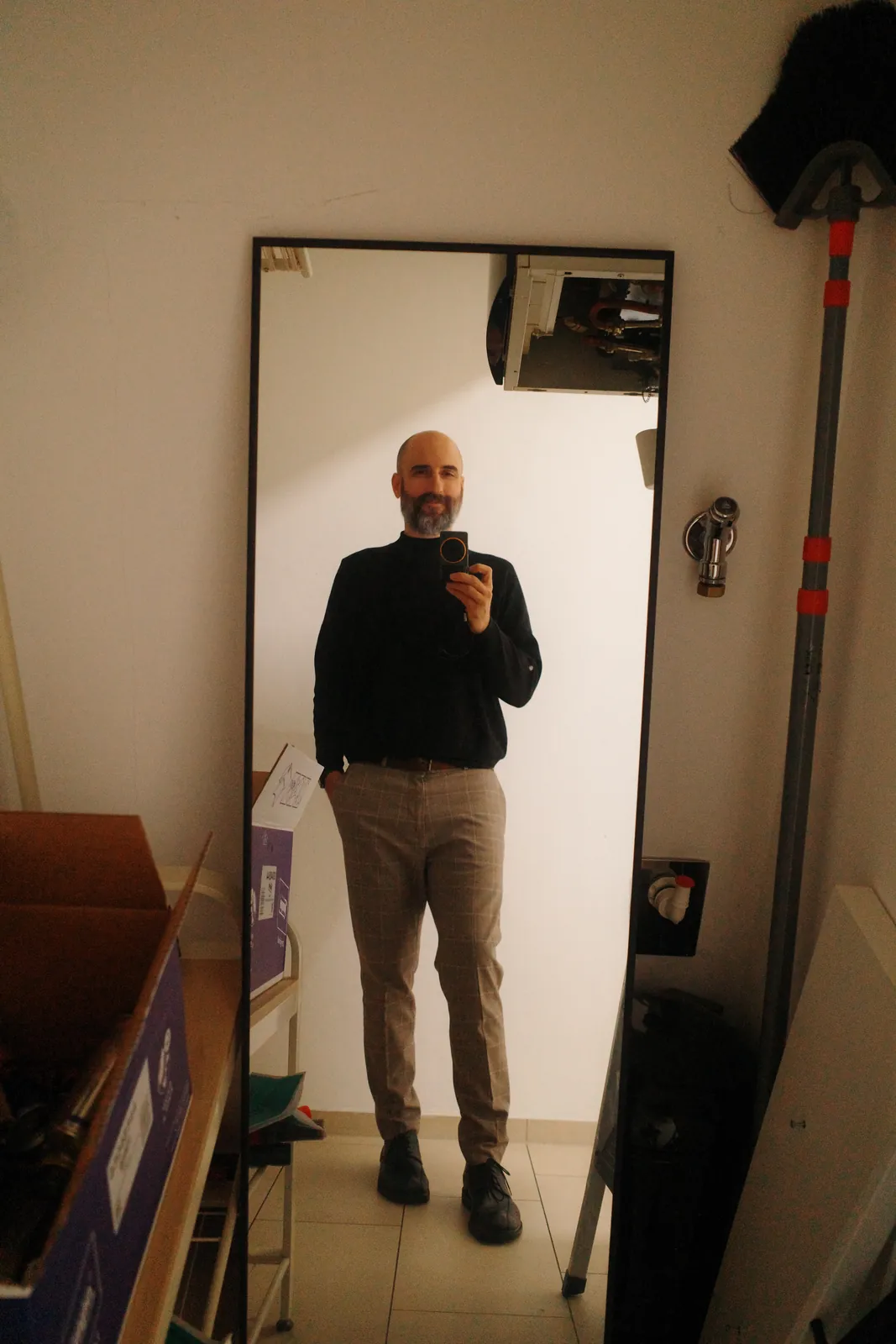 Selbstporträt in einem Standspiegel in einem Abstellraum, ganze Figur, Kamera in Brusthöhe.