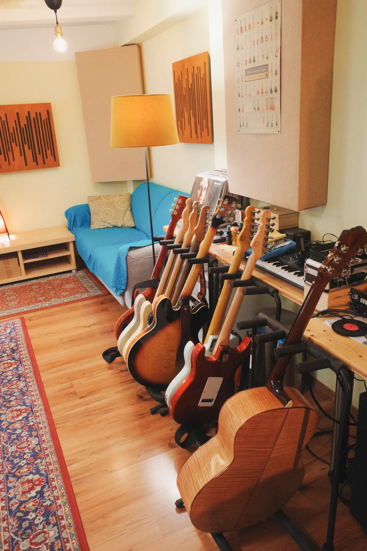 Eine Reihe E-Gitarren, Bässe und eine Akustikgitarre auf Ständern neben dem Sofa im Regieraum.